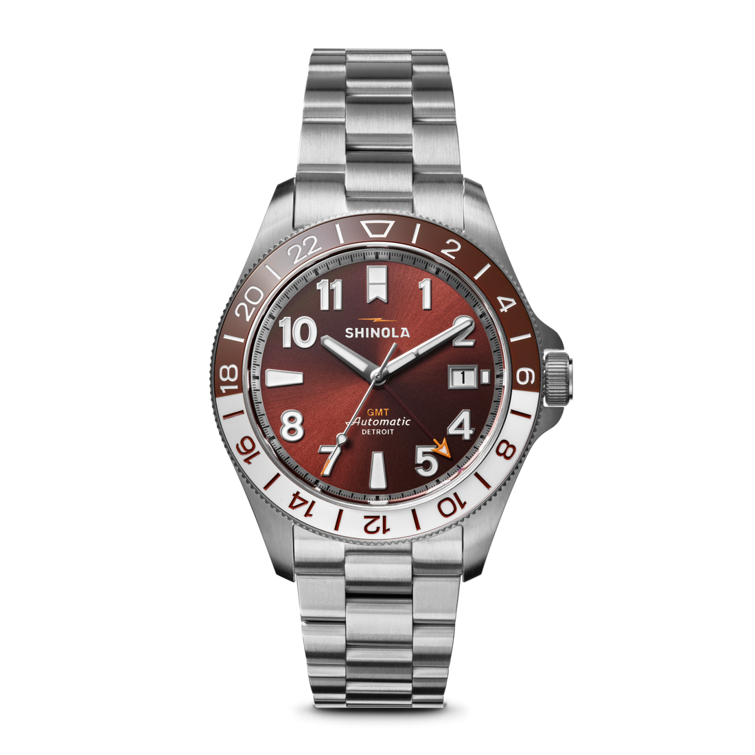 The Shinola Monster GMT Automatic Watch - Whiskey features a stainless steel case, metallic red-brown dial, silver and white hour markers, date at 3 o’clock, 24-hour GMT bezel, and a silver link bracelet.